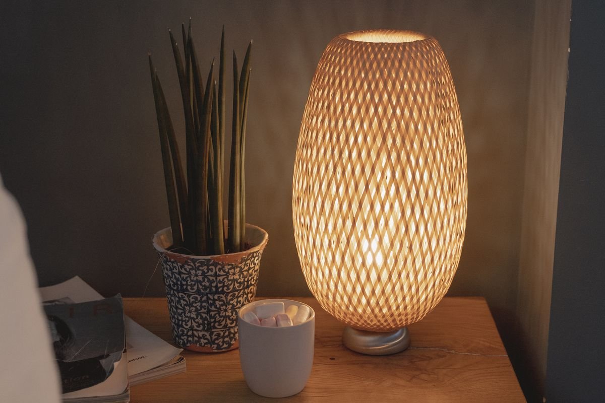 Woven table lamp with potted plant casting a warm cozy glow on a nightstand