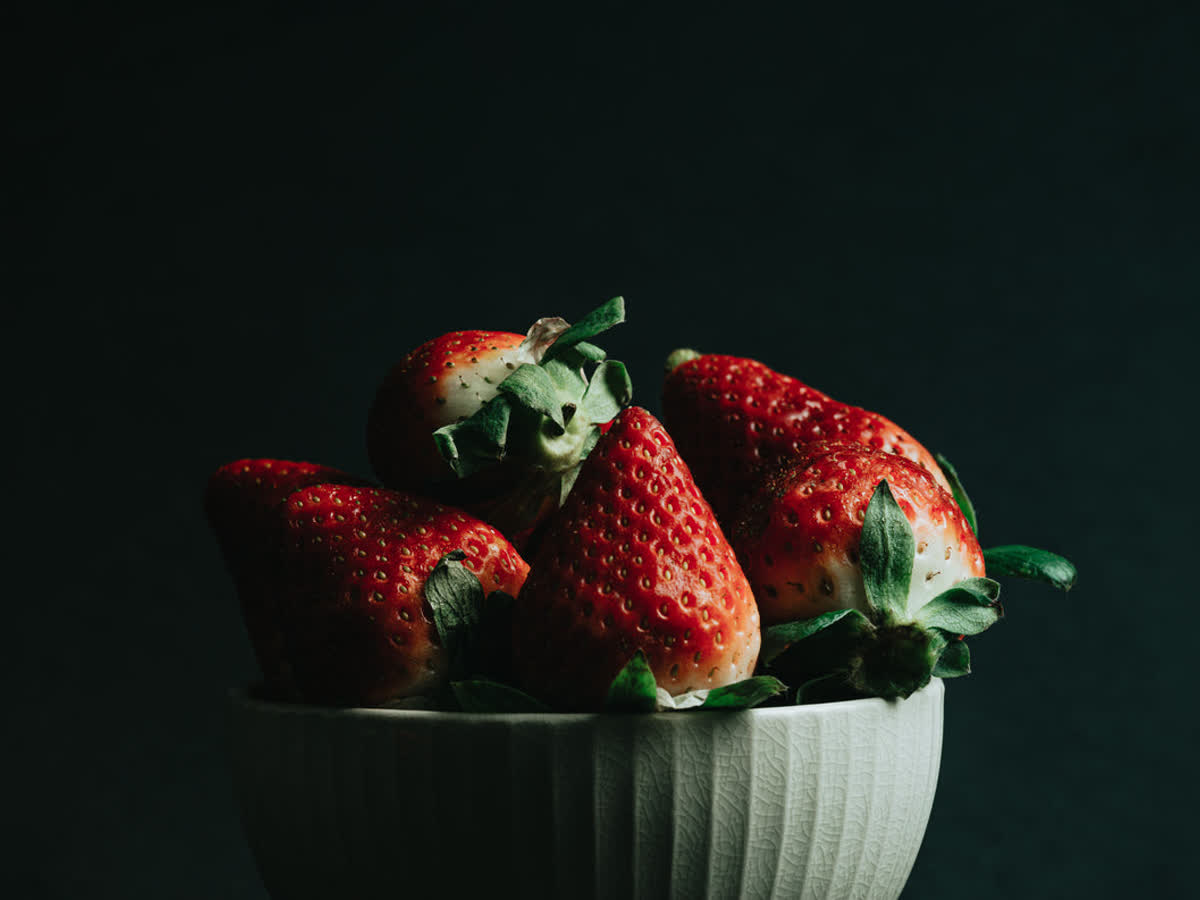 Ripe red strawberries in a white bowl on a dark background under high R9 LED lighting showing fully saturated red skin