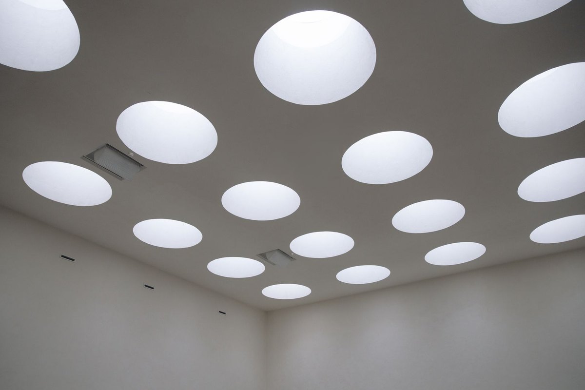 Ceiling of a room read as a field of round downlight apertures of different sizes, showing how aperture area affects apparent brightness