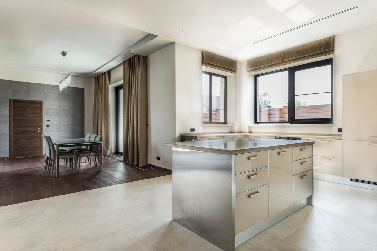Minimal kitchen with a stone island counter lit from a flat ceiling, a layout where task light falls from above and behind the standing position
