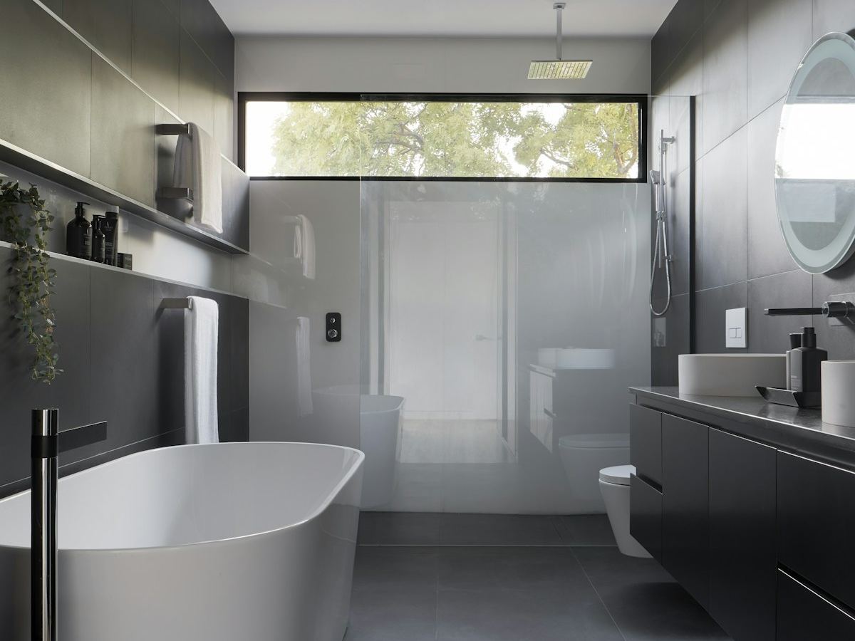 Minimal modern glass house bathroom with dark tiles and a long horizontal window lit by glare-free lighting