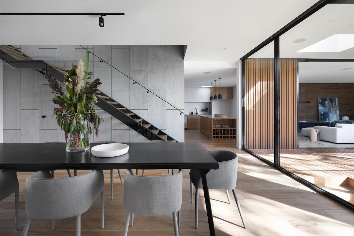 Modern glass house dining area with track lighting and floor-to-ceiling glass walls showing low-glare illumination