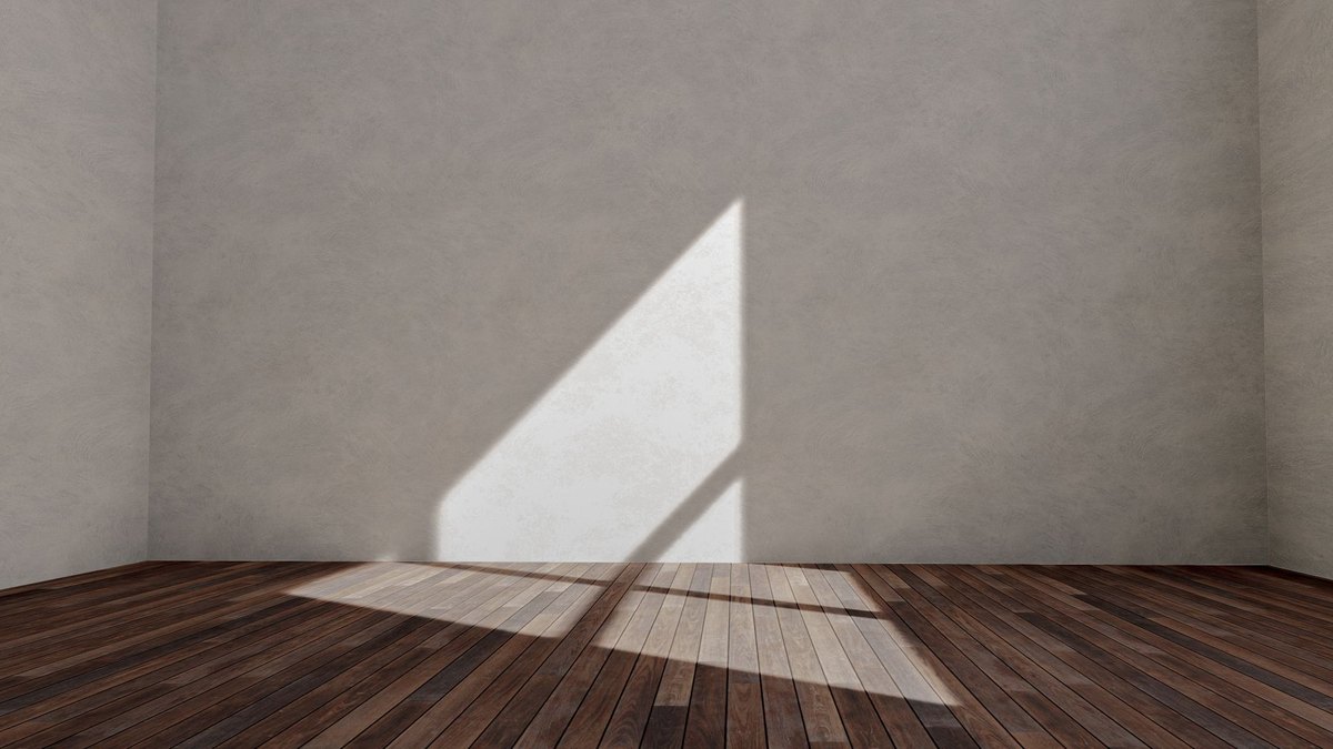 Sunlit empty room with wooden flooring and a shadowed wall before track lighting is installed