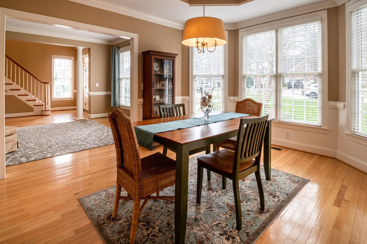 Sunlit dining room with a wooden table and wicker chairs showing the track light spacing used over a dining table
